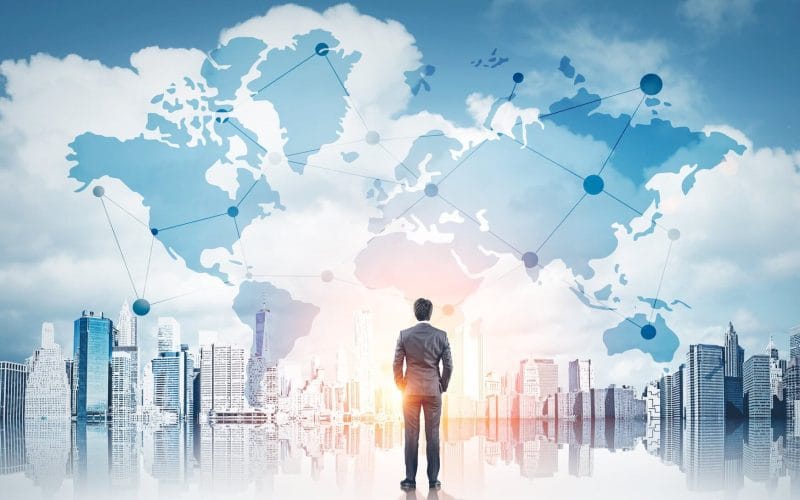 Dal rischio all’opportunità: come le PMI possono crescere in un mercato che cambia. Uomo in abito elegante osserva un panorama urbano con mappa globale sovrapposta, simbolo di connessioni internazionali, reti finanziarie e opportunità di business globali.