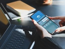PMI e accesso al credito: perché il lending digitale sta cambiando le regole del gioco. Donna utilizza un’app di online banking su smartphone accanto a un laptop, simbolo della digitalizzazione finanziaria per PMI e liberi professionisti.