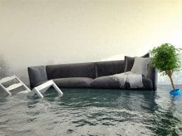 Assicurare il futuro: l’obbligo di copertura contro i disastri naturali. Interno di un’abitazione allagata con divano, sedie e pianta sommersi dall’acqua: simbolo dei danni da alluvione e della necessità di protezione assicurativa.
