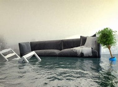 Assicurare il futuro: l’obbligo di copertura contro i disastri naturali. Interno di un’abitazione allagata con divano, sedie e pianta sommersi dall’acqua: simbolo dei danni da alluvione e della necessità di protezione assicurativa.