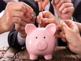 Crowdlending: come la tecnologia sta democratizzando l’accesso al credito e creando. Mani di più persone inseriscono monete in un salvadanaio rosa, simbolo del crowdlending e del finanziamento collettivo alle PMI. nuove opportunità di investimento