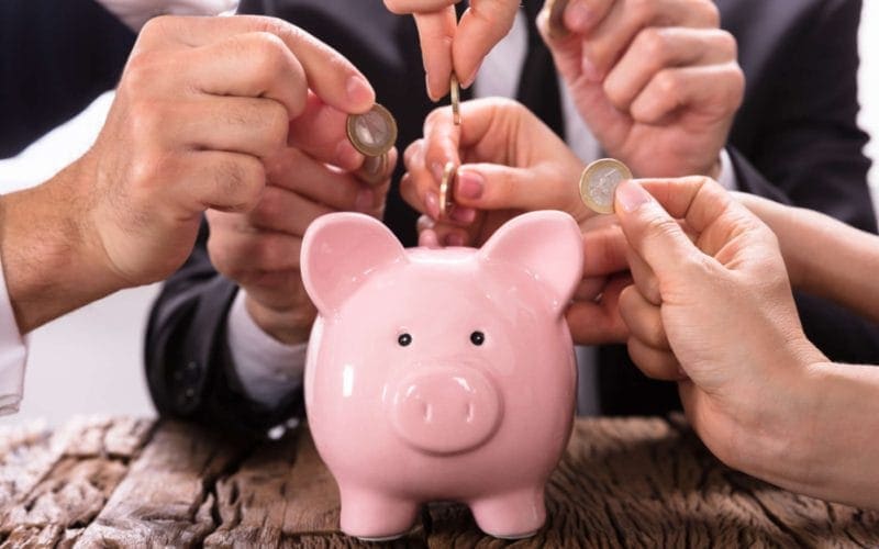 Crowdlending: come la tecnologia sta democratizzando l’accesso al credito e creando. Mani di più persone inseriscono monete in un salvadanaio rosa, simbolo del crowdlending e del finanziamento collettivo alle PMI. nuove opportunità di investimento