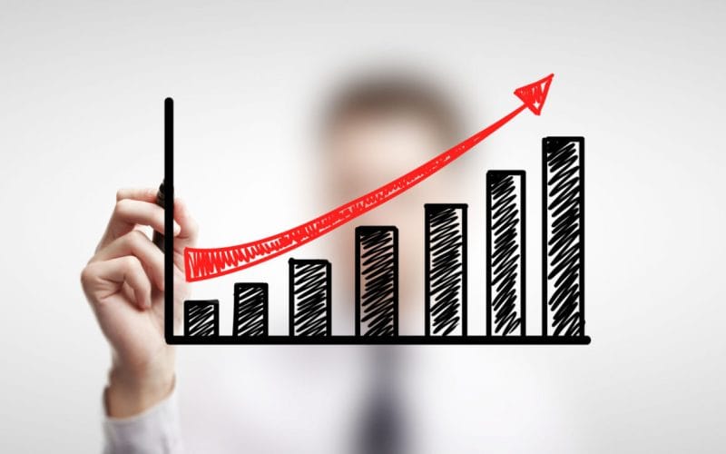 Finanza alternativa: opportunità e rischi per le PMI in cerca di liquidità. Mano disegna un grafico a barre in crescita con freccia rossa ascendente, simbolo di crescita finanziaria e successo di soluzioni alternative di investimento.