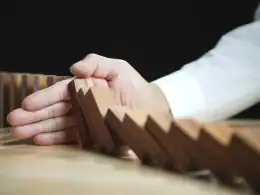 Credito d’impresa: come scegliere tra prestito bancario, factoring e leasing operativo. Una mano ferma la caduta di tessere di domino in legno: simbolo della gestione del rischio e del ruolo del credito d’impresa nella prevenzione di crisi aziendali.