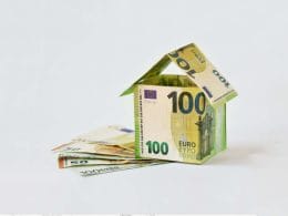 Crowdlending e cessione dei crediti fiscali: una nuova frontiera della finanza alternativa. Casa costruita con banconote da 100 euro su sfondo bianco, simbolo del finanziamento immobiliare tramite crowdlending e cessione dei crediti fiscali.