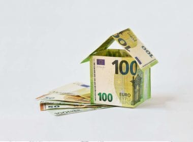Crowdlending e cessione dei crediti fiscali: una nuova frontiera della finanza alternativa. Casa costruita con banconote da 100 euro su sfondo bianco, simbolo del finanziamento immobiliare tramite crowdlending e cessione dei crediti fiscali.