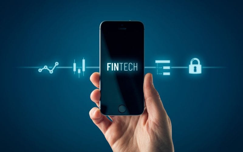 Tecnologia e finanza: l’impatto dell’intelligenza artificiale sulle decisioni economiche delle imprese. Mano tiene uno smartphone con la scritta “FINTECH” sullo schermo; intorno al dispositivo icone digitali che rappresentano dati, sicurezza e analisi finanziaria.