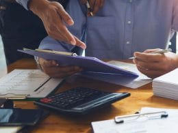 Il factoring spiegato semplice: liberare liquidità dalle fatture senza rischi. Due professionisti esaminano grafici e documenti finanziari su una scrivania con calcolatrice, penne e fascicoli, simbolo di consulenza e pianificazione aziendale.