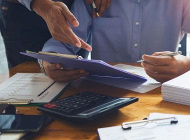 Il factoring spiegato semplice: liberare liquidità dalle fatture senza rischi. Due professionisti esaminano grafici e documenti finanziari su una scrivania con calcolatrice, penne e fascicoli, simbolo di consulenza e pianificazione aziendale.
