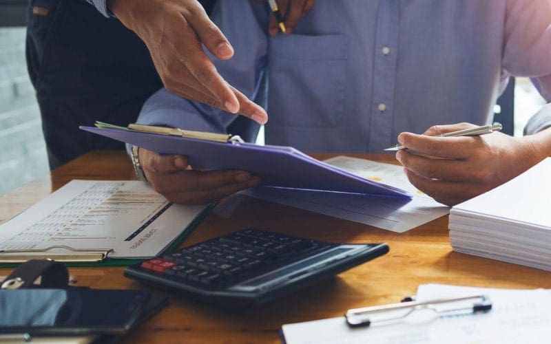 Il factoring spiegato semplice: liberare liquidità dalle fatture senza rischi. Due professionisti esaminano grafici e documenti finanziari su una scrivania con calcolatrice, penne e fascicoli, simbolo di consulenza e pianificazione aziendale.