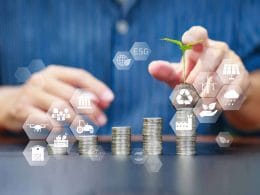 Mani posano una piantina su una pila di monete con icone ESG, a simboleggiare l’integrazione della sostenibilità nei criteri di accesso al credito aziendale.