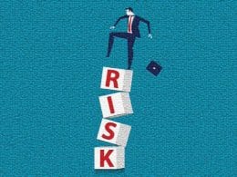 Bancabilità cercasi: il nuovo paradosso delle imprese italiane. Un uomo d’affari sta per cadere da una pila instabile di blocchi con la scritta “RISK”, metafora visiva del rischio d’impresa e della fragilità delle decisioni sbagliate.