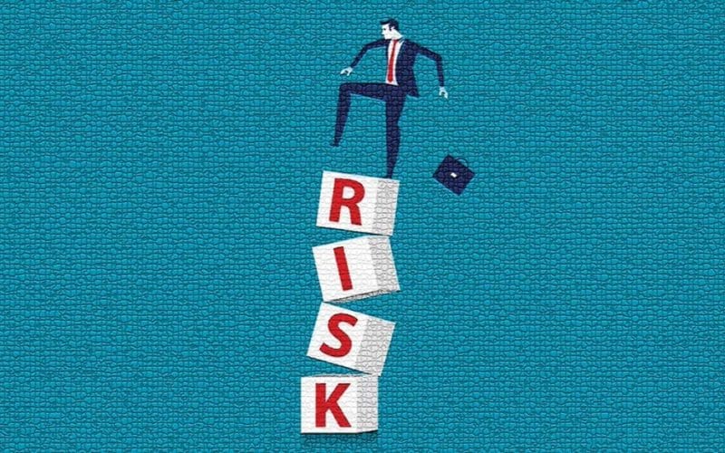 Bancabilità cercasi: il nuovo paradosso delle imprese italiane. Un uomo d’affari sta per cadere da una pila instabile di blocchi con la scritta “RISK”, metafora visiva del rischio d’impresa e della fragilità delle decisioni sbagliate.