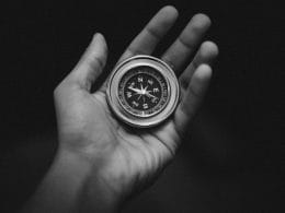 Educazione finanziaria, la bussola per navigare tra scelte, rischi e opportunità. Mano che tiene una bussola su sfondo nero, simbolo dell’educazione finanziaria come guida nelle decisioni economiche complesse.