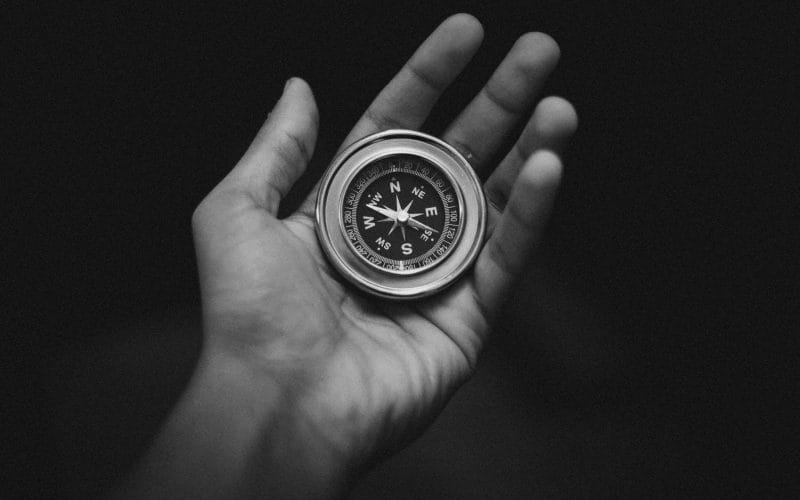 Educazione finanziaria, la bussola per navigare tra scelte, rischi e opportunità. Mano che tiene una bussola su sfondo nero, simbolo dell’educazione finanziaria come guida nelle decisioni economiche complesse.