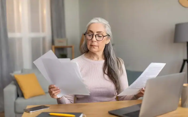 L’impatto del part-time sulla posizione contributiva e le possibili soluzioni per tutelare il diritto a pensione. Donna matura con capelli grigi e occhiali analizza documenti davanti a un computer portatile, valutando gli effetti del lavoro part-time sulla sua pensione.