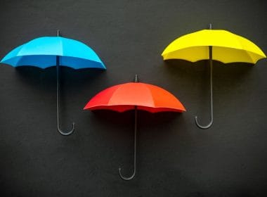 La differenza tra polizza vita e polizza infortuni: facciamo chiarezza. Tre ombrelli colorati — uno blu, uno rosso e uno giallo — su sfondo nero, simbolo visivo di protezione, copertura assicurativa e gestione dei rischi.