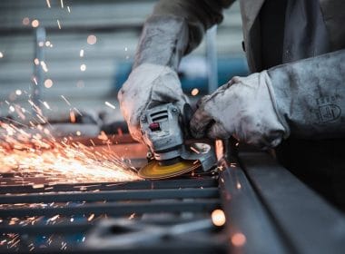 Lavori usuranti e pensione: quali possibilità di uscita anticipata per chi svolge attività particolarmente faticose? Operaio metalmeccanico con guanti protettivi utilizza una smerigliatrice, producendo scintille, simbolo di lavoro usurante e attività gravose ai fini pensionistici.