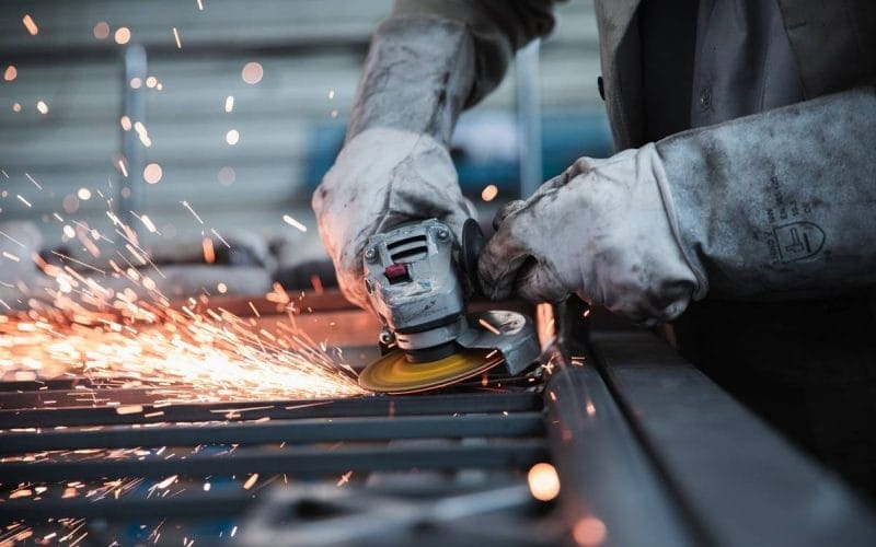 Lavori usuranti e pensione: quali possibilità di uscita anticipata per chi svolge attività particolarmente faticose? Operaio metalmeccanico con guanti protettivi utilizza una smerigliatrice, producendo scintille, simbolo di lavoro usurante e attività gravose ai fini pensionistici.