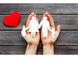 Le 5 polizze base che ogni famiglia dovrebbe valutare. Due mani che sorreggono una sagoma di famiglia con genitori e bambini, accanto a un cuore rosso su sfondo in legno: simbolo della protezione familiare e dell’assicurazione sulla vita.