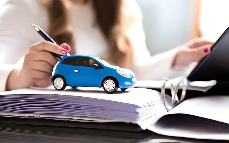 L’assicurazione auto in Italia: dalle origini alla rivoluzione digitale. Modellino di auto blu su un fascicolo di documenti, con una donna che firma o consulta un contratto, simbolo di leasing, finanziamenti auto o noleggio a lungo termine.