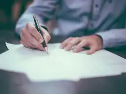 Contributi figurativi gratuiti: quando è possibile ottenerli e quali periodi si possono valorizzare. Persona che firma documenti ufficiali con penna su scrivania, simbolo di riconoscimento dei contributi figurativi gratuiti per la pensione.