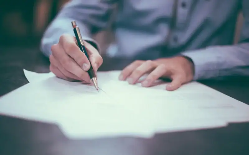 Contributi figurativi gratuiti: quando è possibile ottenerli e quali periodi si possono valorizzare. Persona che firma documenti ufficiali con penna su scrivania, simbolo di riconoscimento dei contributi figurativi gratuiti per la pensione.