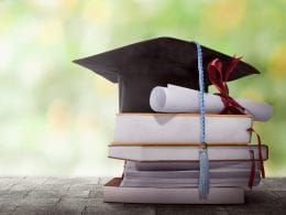 Riscatto della laurea: il riscatto ordinario conviene davvero? Pile di libri con tocco accademico e diploma arrotolato: simbolo del riscatto della laurea per ottenere anni contributivi validi per la pensione.