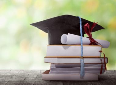 Riscatto della laurea: il riscatto ordinario conviene davvero? Pile di libri con tocco accademico e diploma arrotolato: simbolo del riscatto della laurea per ottenere anni contributivi validi per la pensione.
