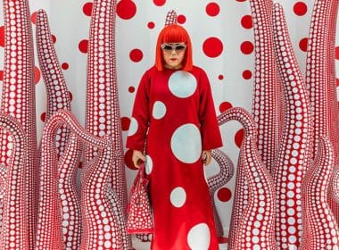 Mercato dell'arte. Donna con parrucca rossa in ambiente immersivo optical rosso e bianco, stile Yayoi Kusama, simbolo dell’arte contemporanea femminile.