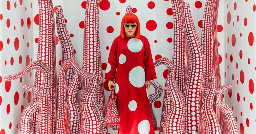 Mercato dell'arte. Donna con parrucca rossa in ambiente immersivo optical rosso e bianco, stile Yayoi Kusama, simbolo dell’arte contemporanea femminile.