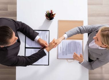 Cessione del credito, guida essenziale. Due professionisti si stringono la mano dopo aver firmato un contratto di cessione del credito, visti dall’alto.