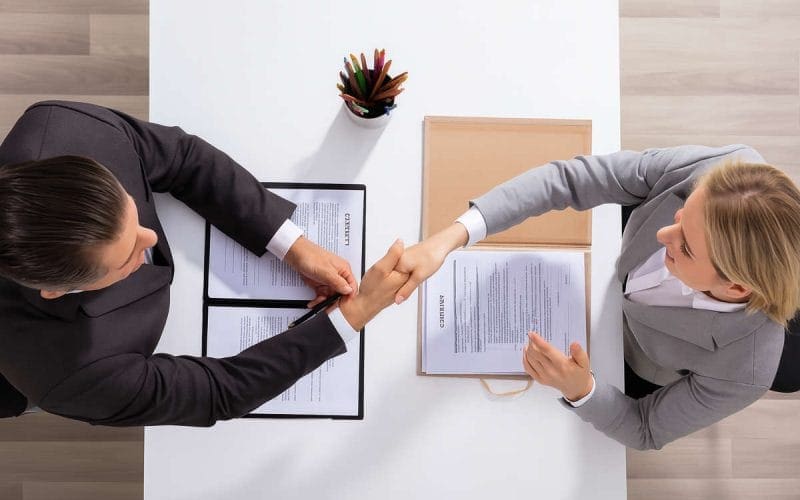 Cessione del credito, guida essenziale. Due professionisti si stringono la mano dopo aver firmato un contratto di cessione del credito, visti dall’alto.