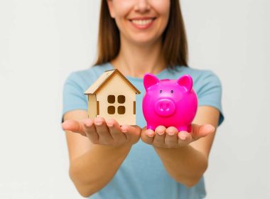 Donna che tiene una casetta in legno e un salvadanaio rosa fucsia, concetto di superbonus crediti in attesa di accettazione.