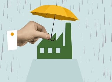Una mano regge un ombrello giallo sopra una fabbrica stilizzata sotto la pioggia, a simboleggiare la protezione offerta dalle assicurazioni catastrofali.