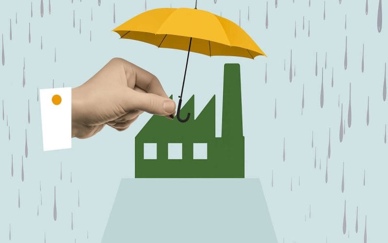 Una mano regge un ombrello giallo sopra una fabbrica stilizzata sotto la pioggia, a simboleggiare la protezione offerta dalle assicurazioni catastrofali.