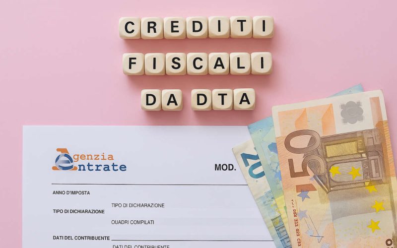 Crediti fiscali da DTA con modulo Agenzia delle Entrate e banconote euro su sfondo rosa, concetto di agevolazioni fiscali.