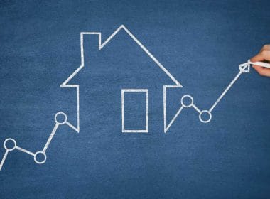 Crowdfunding immobiliare. Grafico a linea crescente con cerchi di raccordo e freccia finale, disegnato con gesso bianco su una lavagna blu, che attraversa una sagoma stilizzata di una casa.