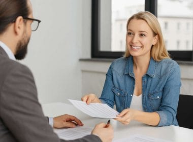 Donna sorridente consegna un documento a un consulente durante un incontro professionale su mandati corporate in ambito di mediazione creditizia.