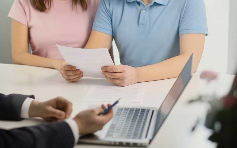 Negoziare meglio con la banca – coppia e consulente durante trattativa su documenti. Coppia che negozia con la banca tenendo documenti davanti a un consulente