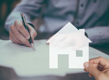 Mano che firma documenti fiscali per bonus casa 2025 con icona di abitazione sovrapposta