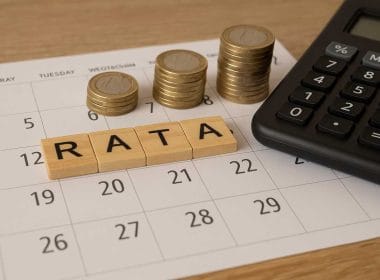 Pila di monete su un calendario accanto a una calcolatrice e blocchi in legno con la scritta “RATA”, simbolo della compensazione fiscale a rate del credito d’imposta Transizione 5.0.