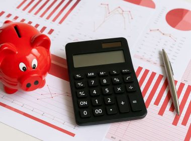 Salvadanaio rosso e calcolatrice su grafici finanziari, simbolo dei contributi figurativi gratuiti per la pensione INPS.