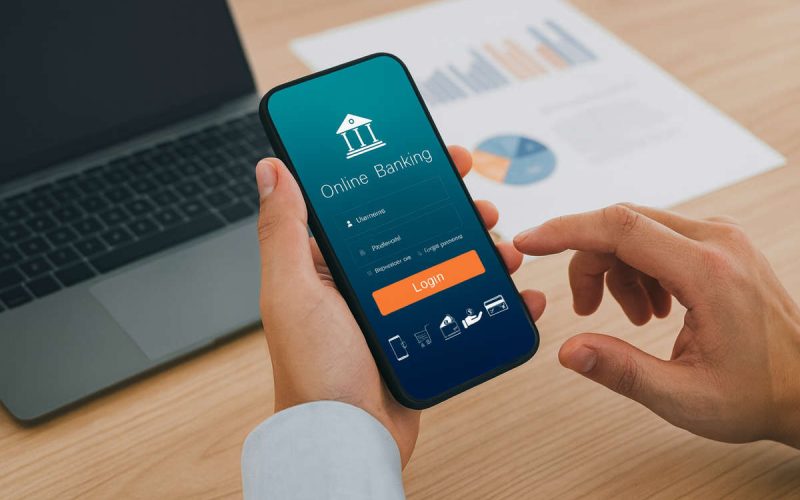 Persona al computer e smartphone con app di online banking, simbolo della guida ABI sui bonifici istantanei e sulla sicurezza dei pagamenti digitali.