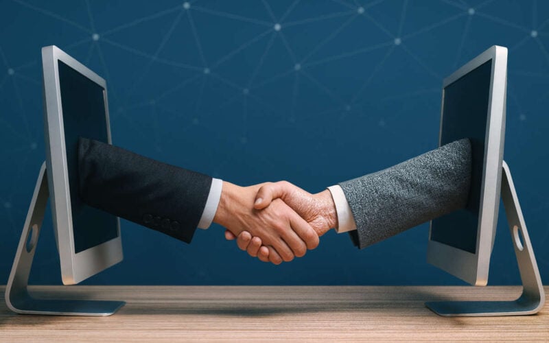 Due persone si stringono la mano attraverso schermi di computer rappresentando accordi digitali nei rischi lending crowdfunding
