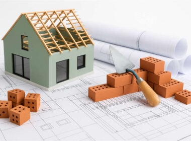Bonus edilizi 2025: modellino casa in ristrutturazione con mattoni, progetti architettonici e strumenti da lavoro per detrazioni fiscali prima casa