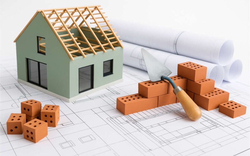 Bonus edilizi 2025: modellino casa in ristrutturazione con mattoni, progetti architettonici e strumenti da lavoro per detrazioni fiscali prima casa