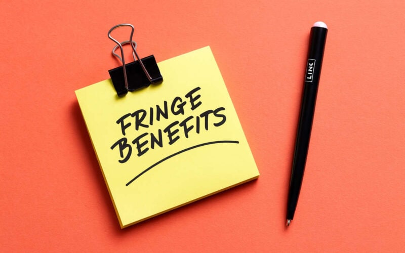 Post-it giallo con scritta Fringe benefit e penna su sfondo rosso corallo