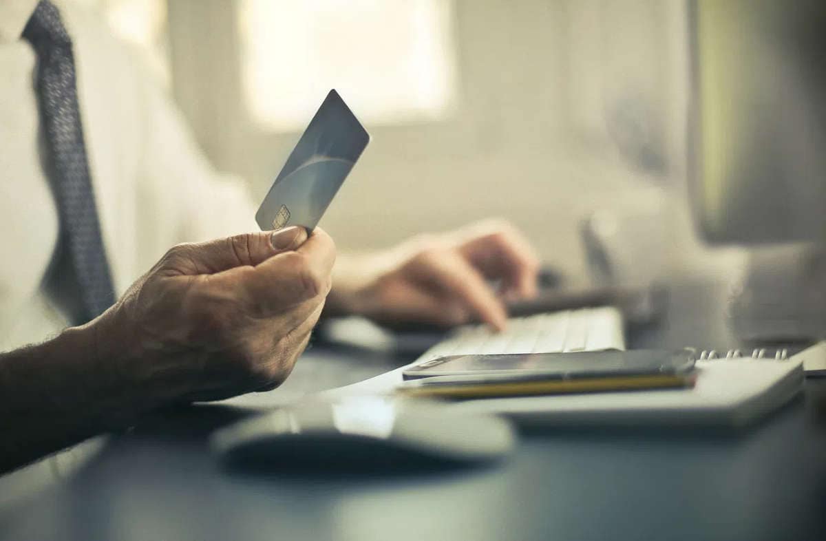 Chiamate truffa dall'estero: come riconoscerle e bloccarle. Uomo al computer con carta di credito in mano, rischio di chiamate truffa dall’estero.