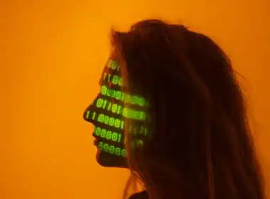 truffe online, profilo femminile con codice binario verde proiettato sul volto su sfondo arancione.